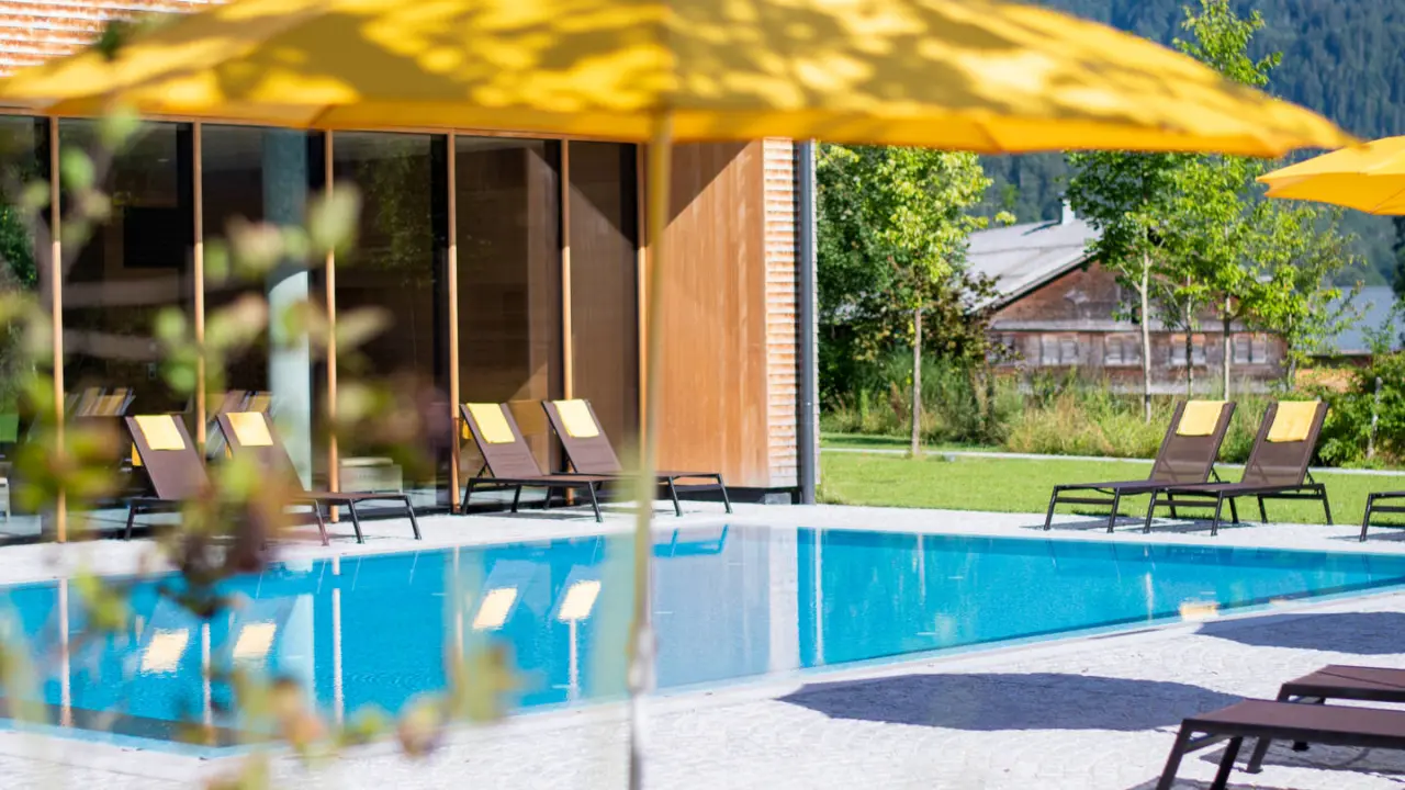 Aussenpool mit bequemen Liegestühlen und gelben Sonnenschirmen im Hotel die Wälderin****s, umgeben von grüner Natur.