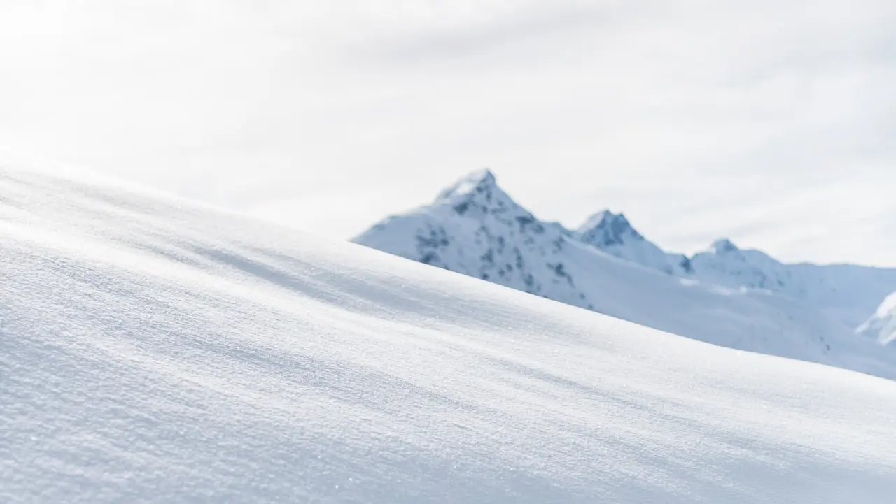 Verschneite Berglandschaft mit sanften Schneehügeln und unscharfen Gipfeln im Hintergrund, nahe dem BelArosa Hotel.