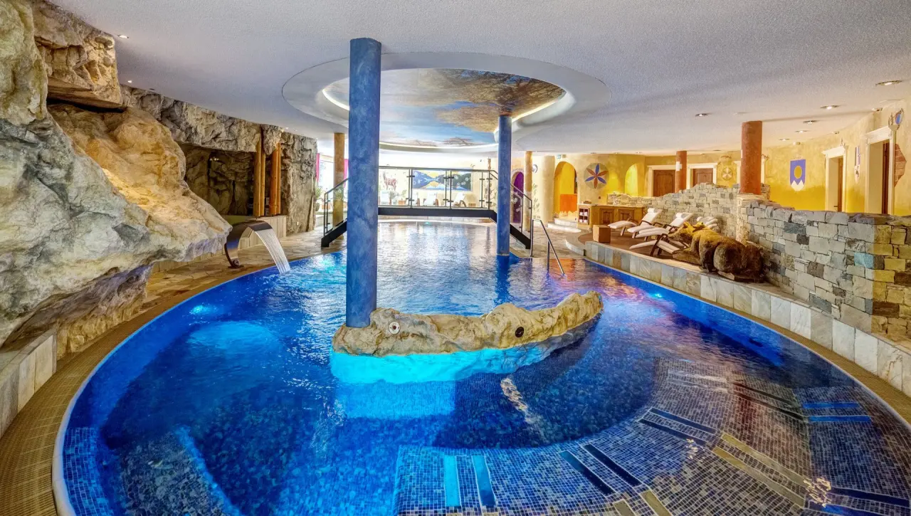 Grosszügiger Innenpool mit Felsenlandschaft und Wasserfall im Wellnessbereich des BelArosa Hotels.