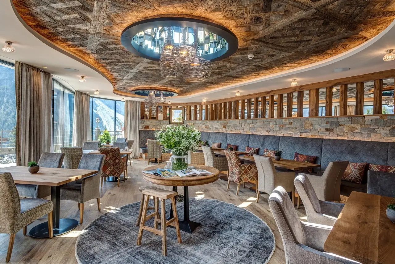 Elegantes Restaurant im BelArosa Hotel mit Panoramablick auf die Berge, gemütlichen Sitzbereichen und stilvoller Einrichtung.