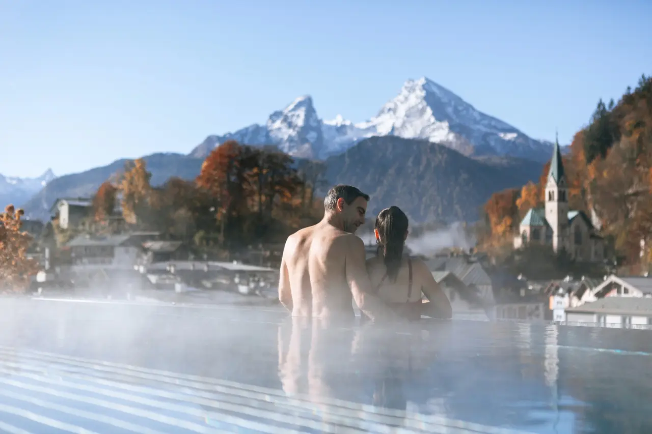 Paar entspannt im Infinity Pool des Hotel EDELWEISS Berchtesgaden mit atemberaubendem Blick auf den Watzmann und Alpenpanorama.
