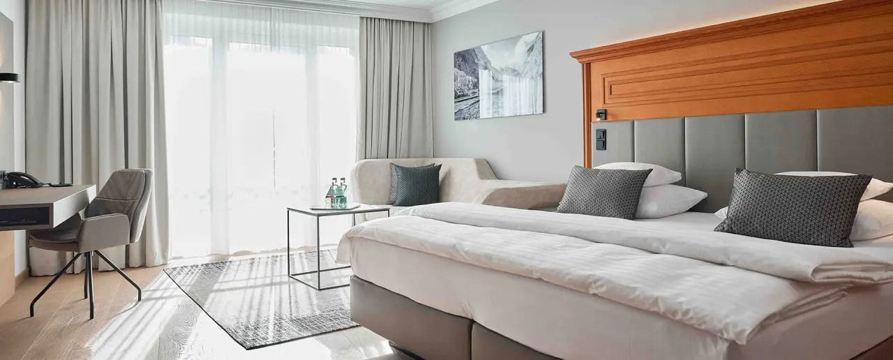 Modernes Hotelzimmer im Hotel EDELWEISS Berchtesgaden mit Doppelbett, Schreibtisch und gemütlichem Sitzbereich.