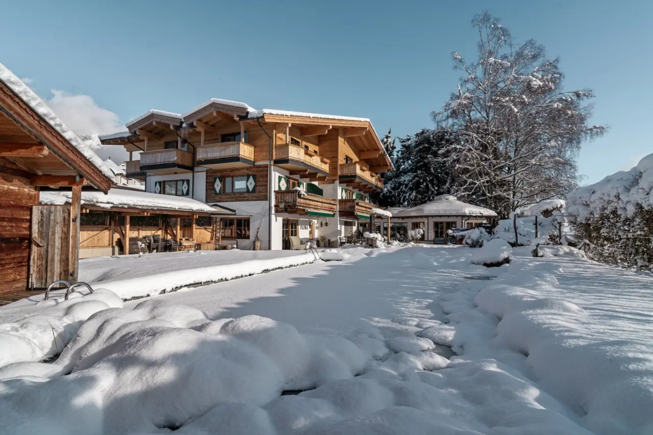 Hotel Hochfilzer im Winter: Traditionelles Alpenhotel mit verschneitem Aussenbereich und Pool unter blauem Himmel.