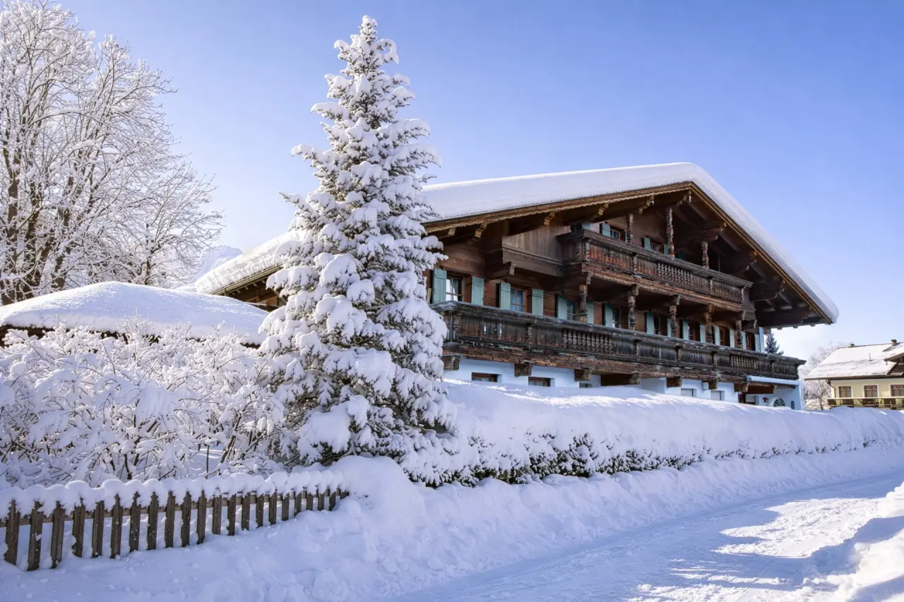 Hotel Hochfilzer im Winter: Traditionelles Holzhotel mit verschneitem Dach und Tannenbaum unter blauem Himmel.