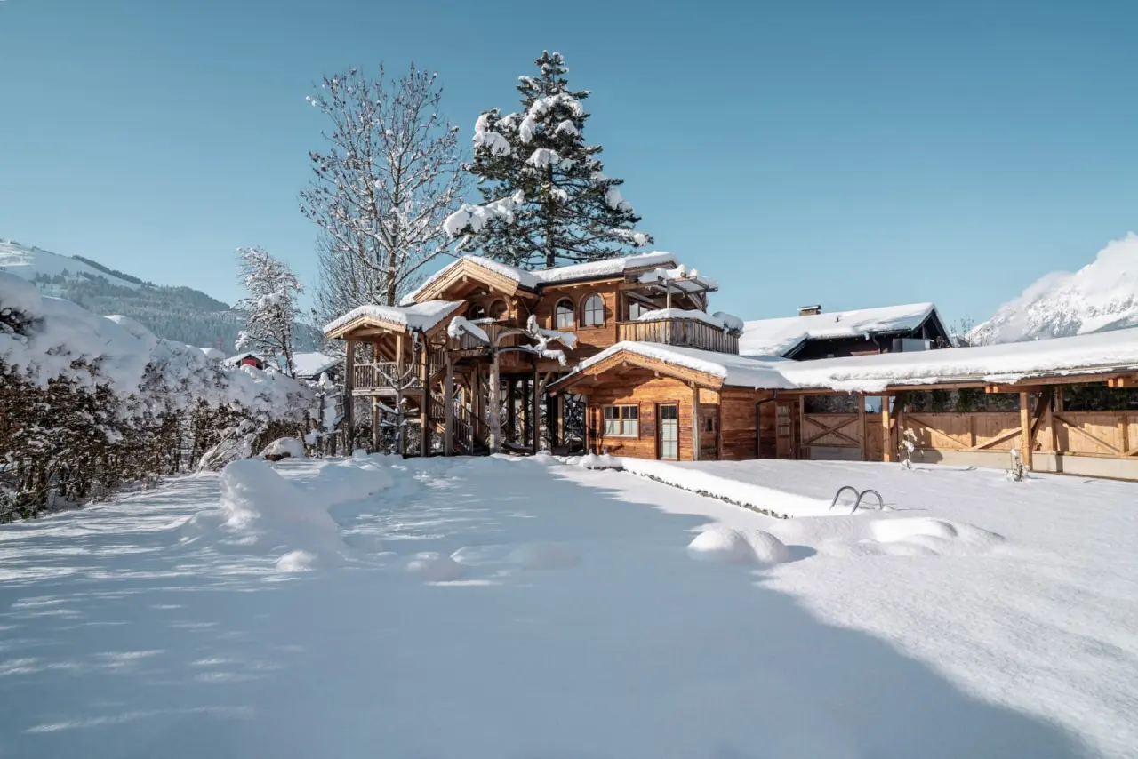 Verschneites Hotel Hochfilzer in den Alpen mit traditioneller Holzarchitektur und blauem Winterhimmel.