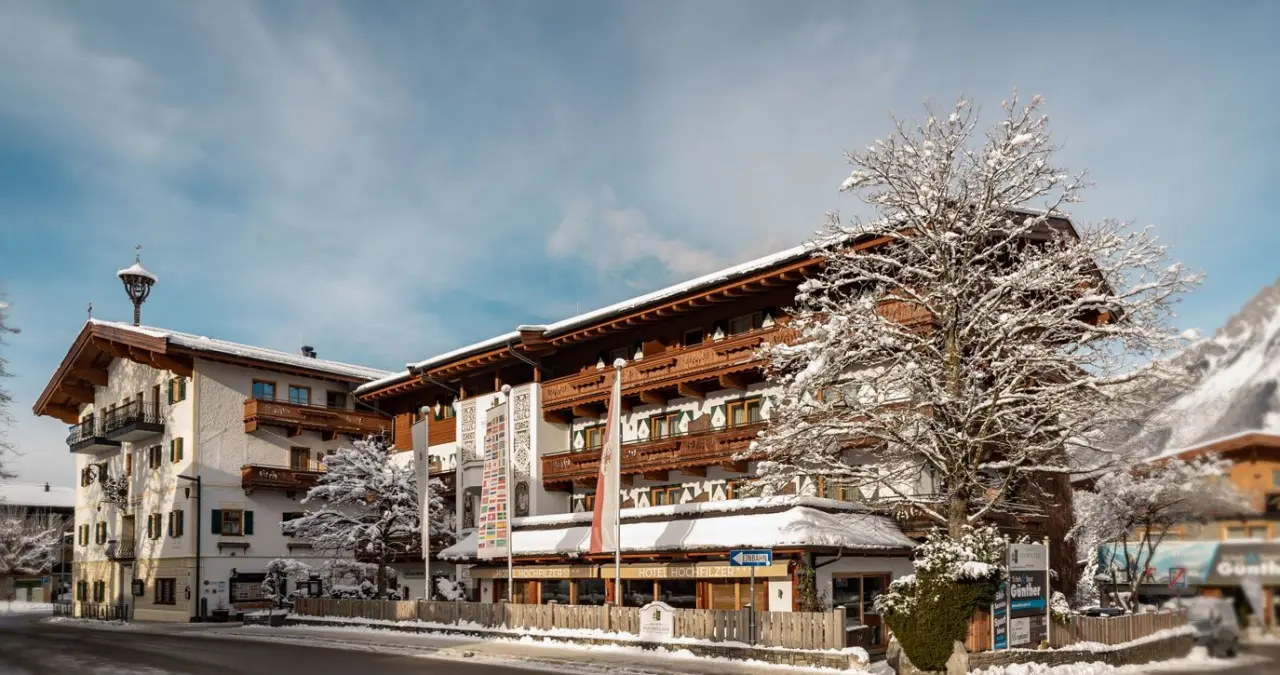 Hotel Hochfilzer in den Kitzbüheler Alpen im Winter, mit verschneiter Fassade und Baum unter blauem Himmel.