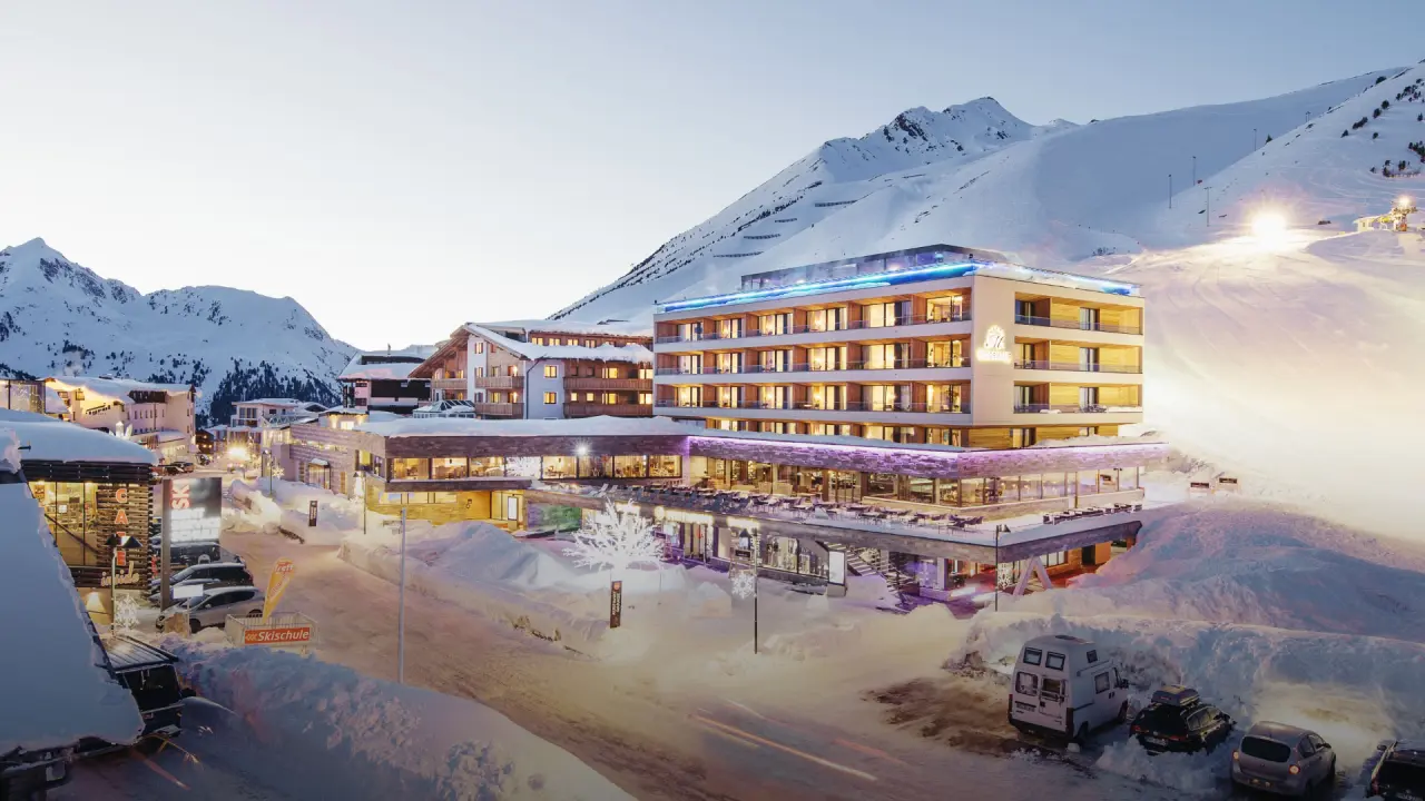 Hotel Mooshaus in verschneiter Alpenlandschaft bei Dämmerung mit beleuchteten Terrassen und Bergblick.