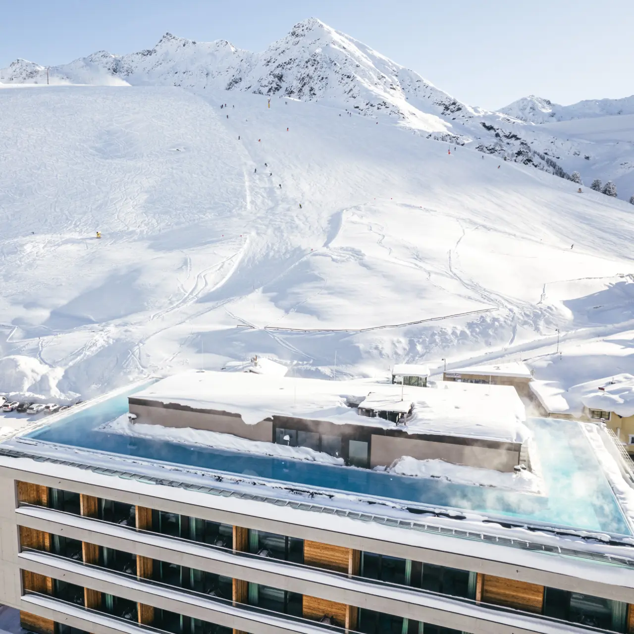Beheizter Infinity Pool des Hotel Mooshaus mit Dampf und Panoramablick auf die verschneiten Alpen und Skipisten.