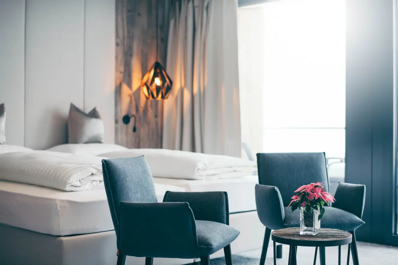 Modernes Hotelzimmer im Hotel Mooshaus mit Doppelbett, gemütlichem Sitzbereich und Blick zum Balkon.
