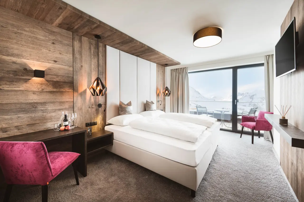 Modernes Doppelzimmer im Hotel Mooshaus mit Holzelementen, Balkon und Panoramablick auf die verschneiten Berge.