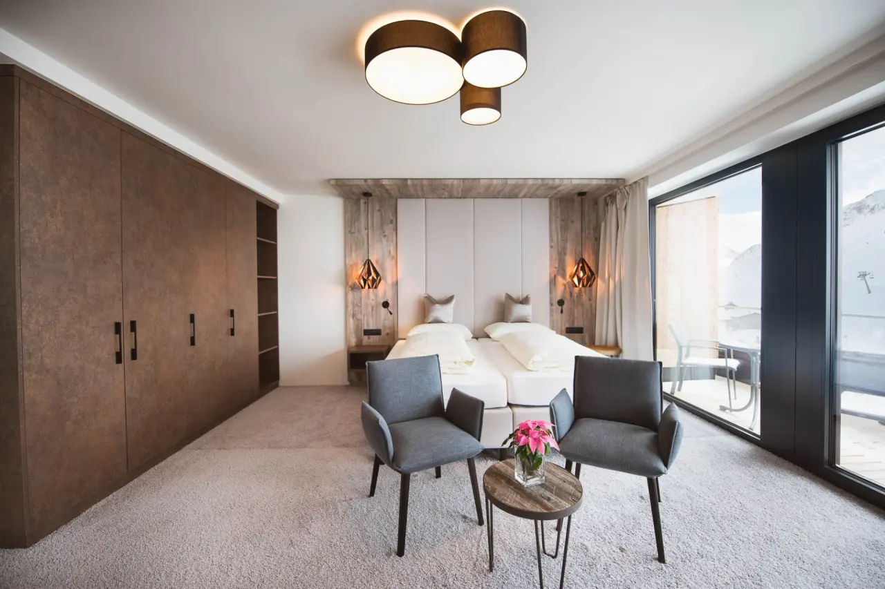 Modernes Doppelzimmer im Hotel Mooshaus mit gemütlichen Sesseln, Holzelementen und Blick auf die verschneite Berglandschaft.