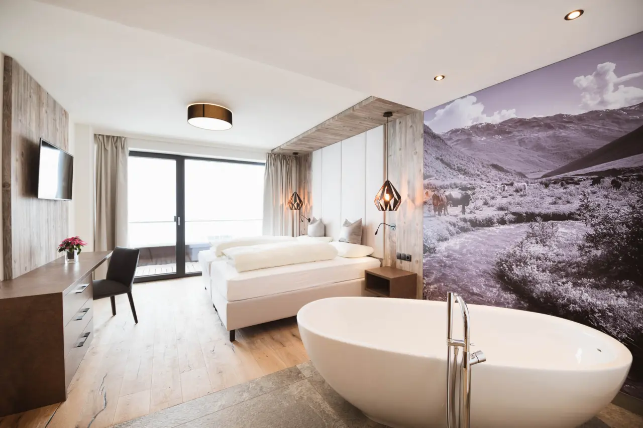 Luxuriöses Hotelzimmer im Hotel Mooshaus mit freistehender Badewanne, Doppelbett und Bergblick-Wandbild.