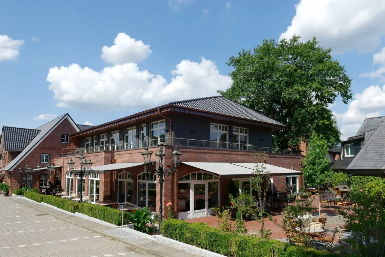 Aussenansicht des Ringhotel Sellhorn mit roter Backsteinfassade, Balkonen und sonniger Terrasse im Gartenbereich.