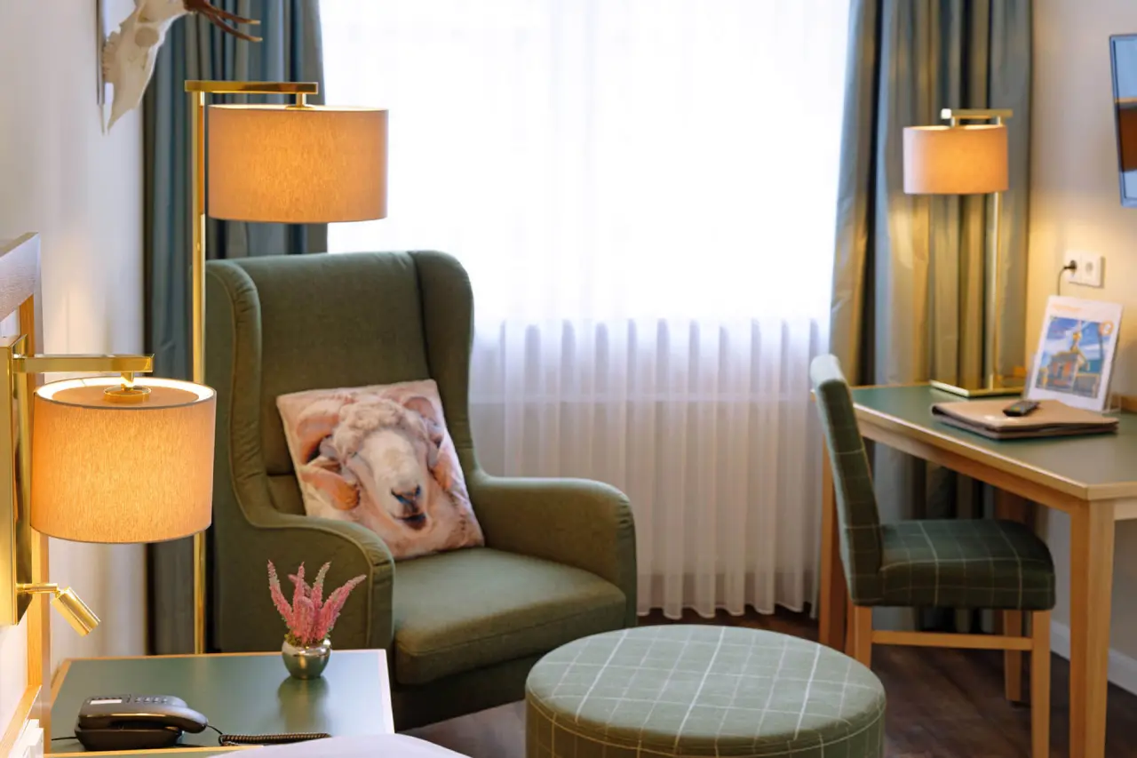 Gemütliche Sitzecke mit Sessel, Hocker und Schreibtisch in einem Hotelzimmer im Ringhotel Sellhorn.