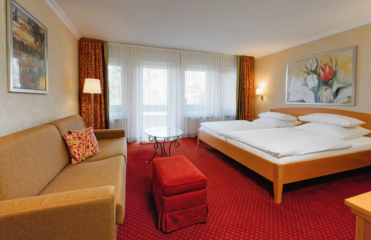 Gemütliches Doppelzimmer mit Sofa, rotem Teppich und großen Fenstern im Ringhotel Sellhorn.