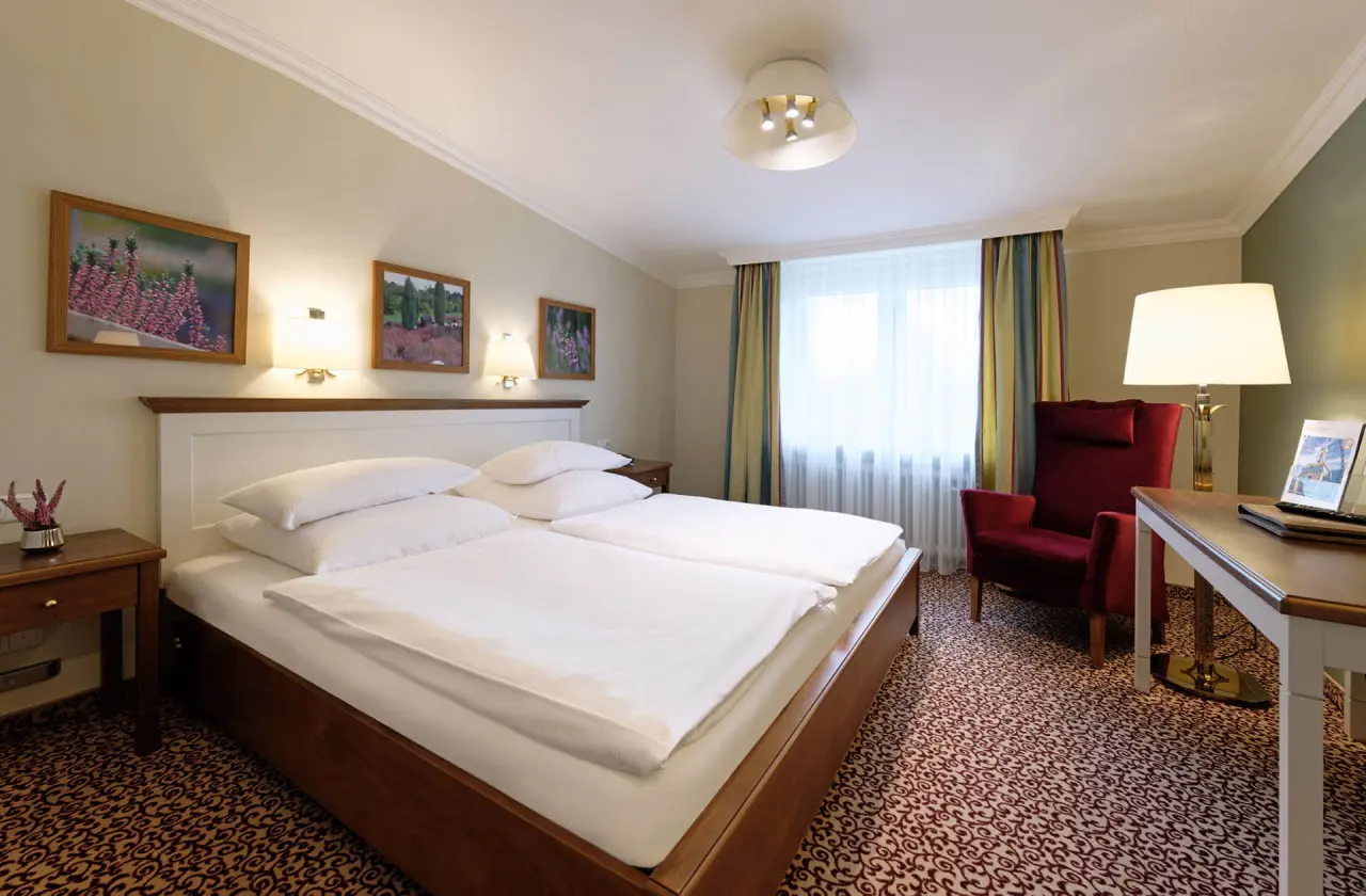 Gemütliches Doppelzimmer im Ringhotel Sellhorn mit bequemen Betten, rotem Sessel und Schreibtisch.