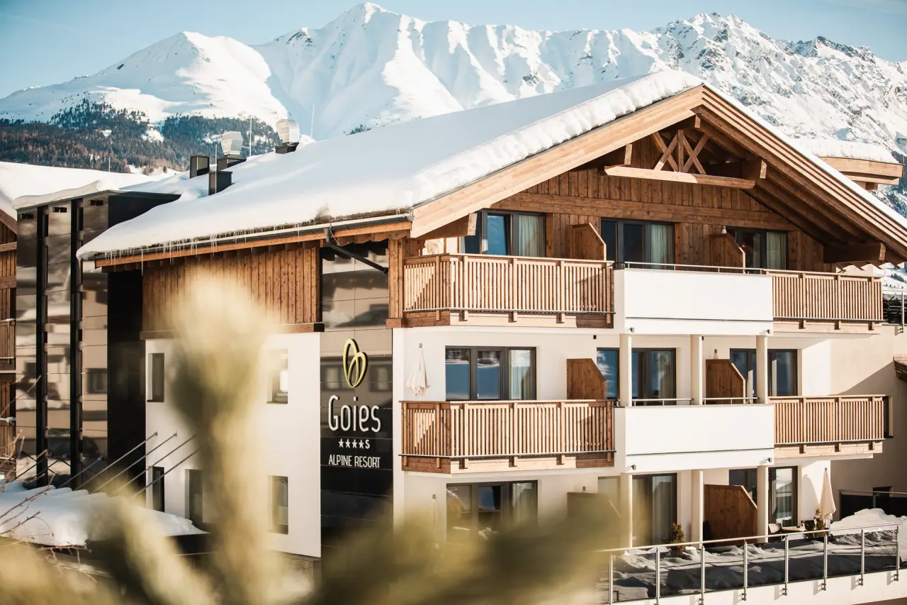 Modernes Alpine Hotel Resort Goies im Winter mit schneebedeckten Bergen im Hintergrund unter blauem Himmel.