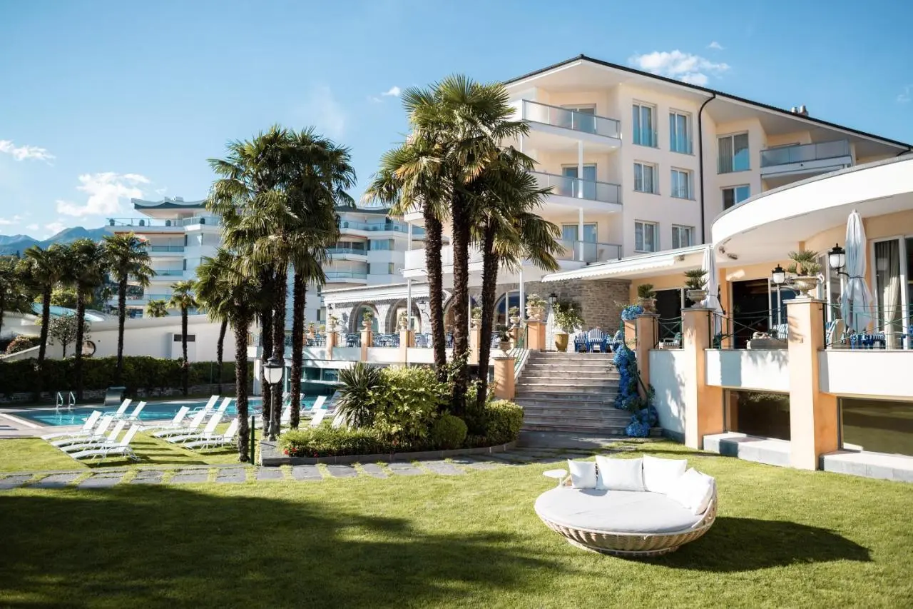 Luxuriöse Aussenansicht des Hotel Eden Roc Ascona mit Pool, Palmen und mediterranem Garten unter blauem Himmel.