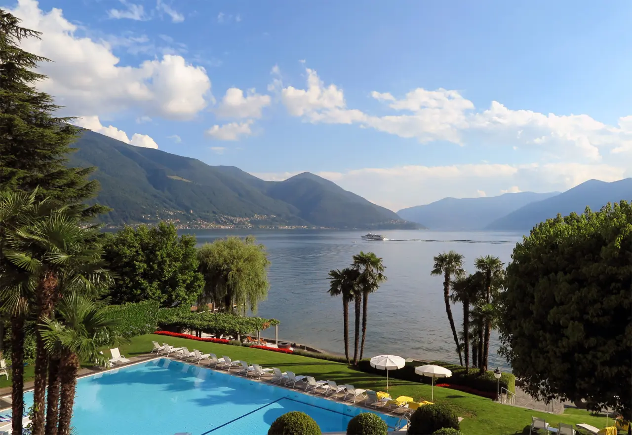 Grosser Aussenpool mit Liegestühlen, Palmen und Blick auf den Lago Maggiore und die Berge im Hotel Eden Roc Ascona.