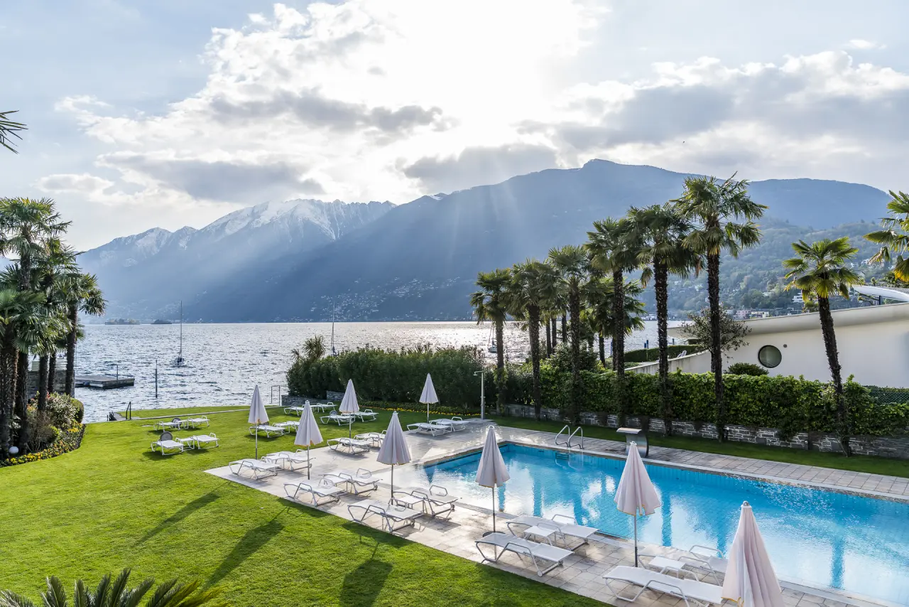 Aussenpool mit Liegestühlen, Palmen und Panoramablick auf den Lago Maggiore und die Berge im Hotel Eden Roc Ascona.
