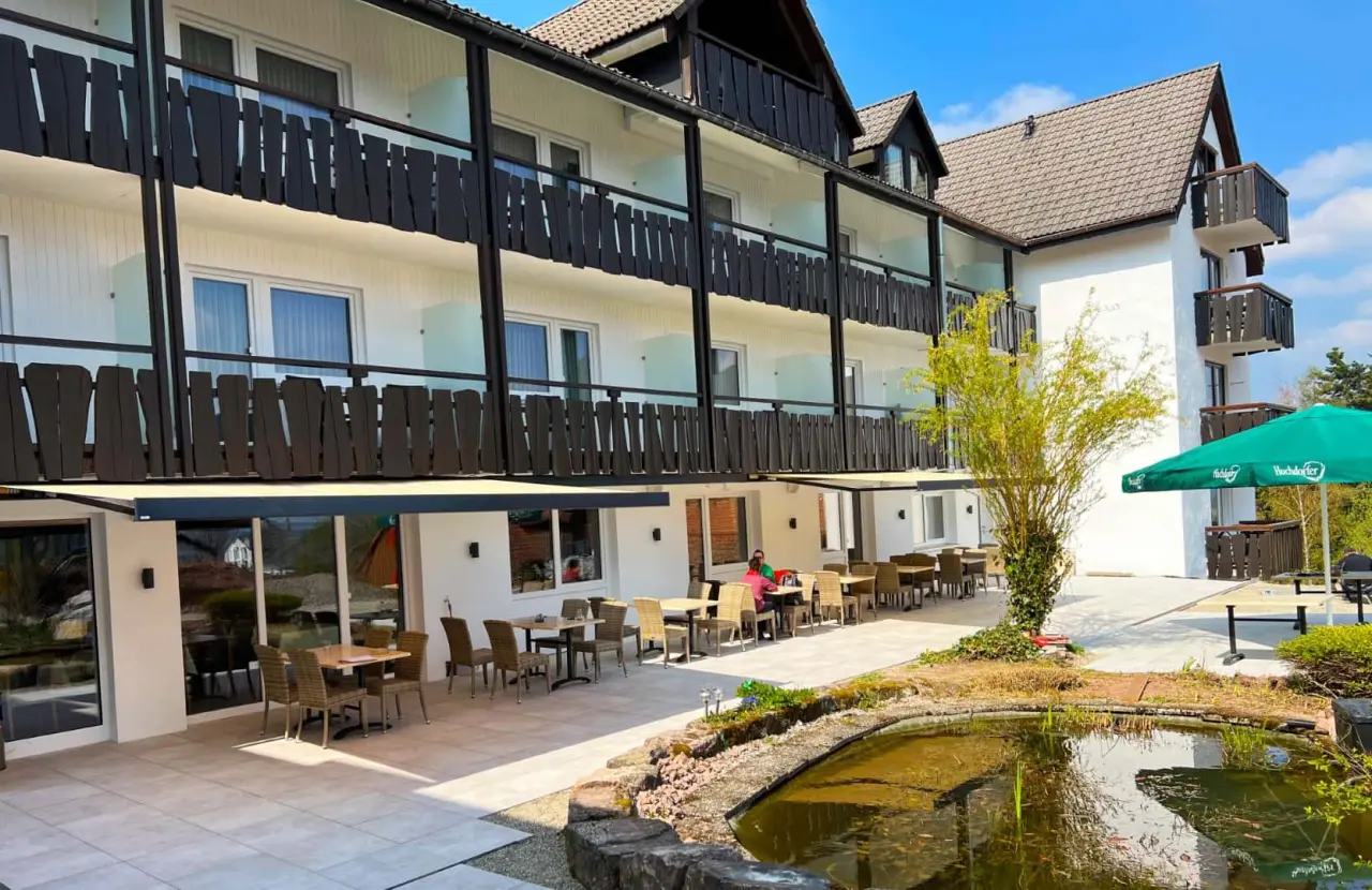 Aussenansicht des Wellnesshotel Hohenrodt mit Sonnenterrasse und Teich im Gartenbereich.
