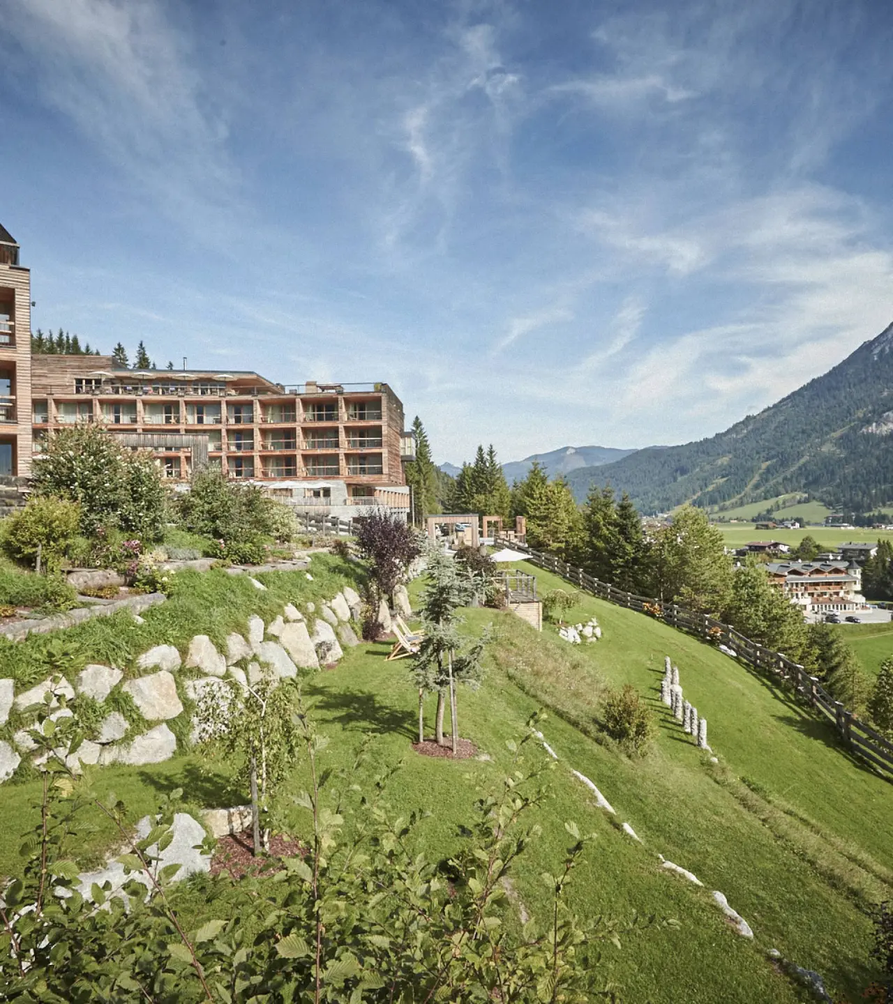 DAS KRONTHALER****S Hotel in den Alpen, umgeben von grünen Hügeln und Wäldern unter blauem Himmel.