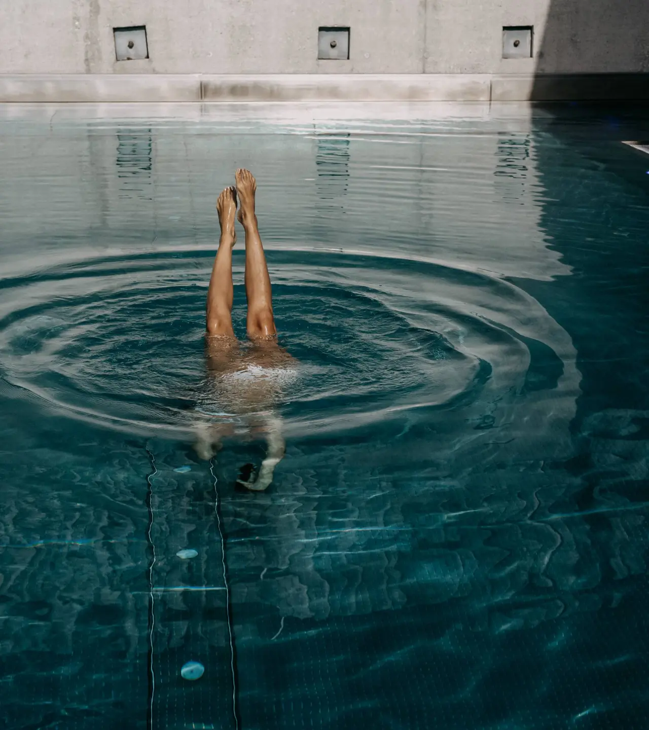 Beine einer Person ragen aus dem Poolwasser im DAS KRONTHALER****S. Moderne Poolanlage für Entspannung und Aktivität.
