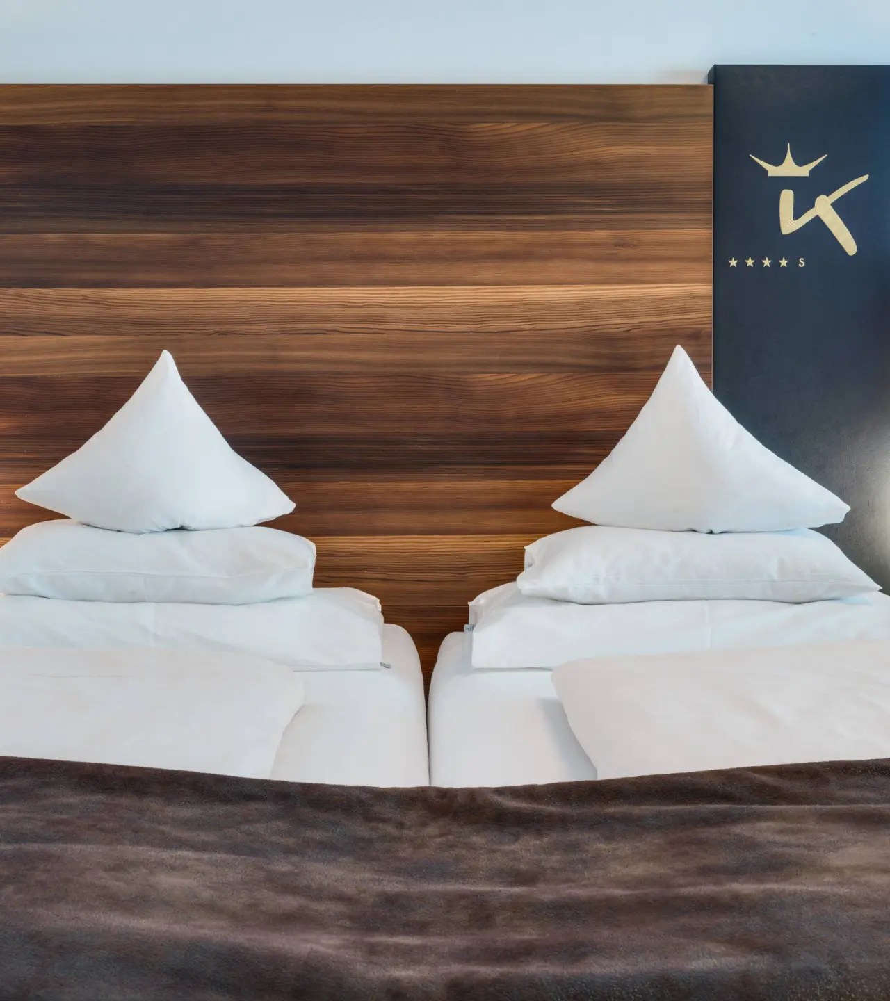 Komfortables Doppelbett mit Holzkopfteil und DAS KRONTHALER****S Logo im Hotelzimmer.