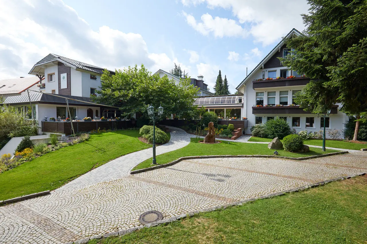 Aussenansicht des Waldhotel Grüner Baum mit gepflegtem Garten, Terrasse und Zufahrt unter blauem Himmel.