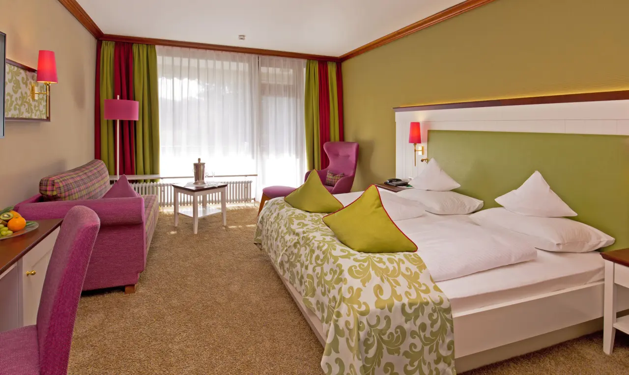 Komfortables Hotelzimmer im Waldhotel Grüner Baum mit Doppelbett, Sitzbereich und farbenfroher Einrichtung.