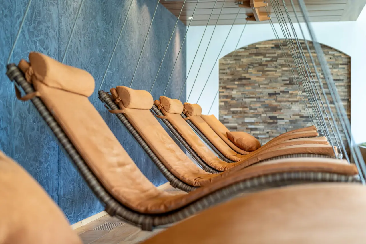 Stilvoller Ruhebereich mit hängenden Relaxliegen und Natursteinwand im Spa des Alpbacherhof****s Mountain & Spa Resort.