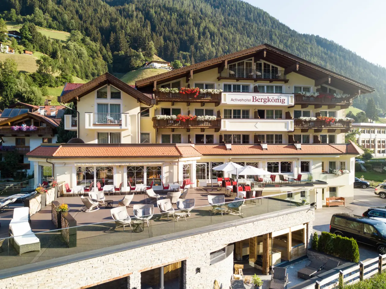Aussenansicht des Activhotel Bergkönig in den Bergen mit Sonnenterrasse, Balkonen und alpiner Landschaft.