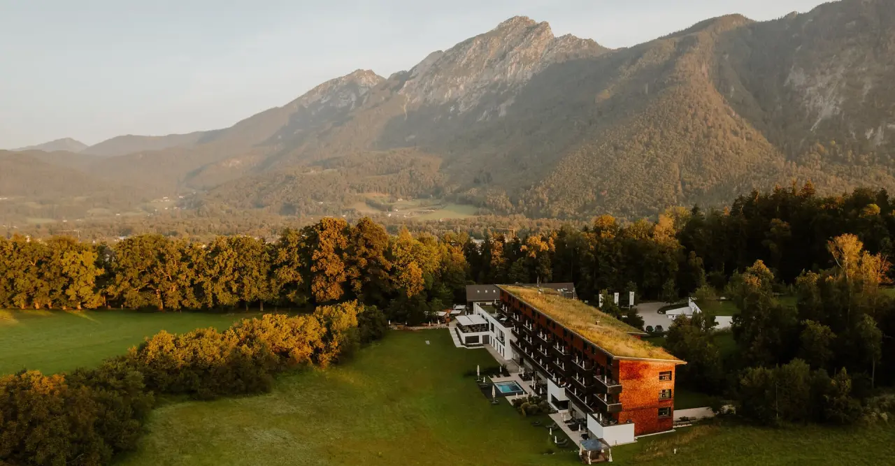Luftaufnahme des Klosterhof - Alpine Hideaway & Spa mit begrüntem Dach und Bergpanorama bei Sonnenuntergang.