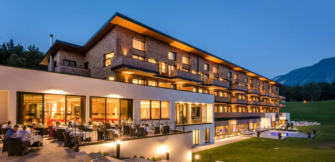 Abendansicht des Klosterhof - Alpine Hideaway & Spa mit beleuchteter Restaurantterrasse, Aussenpool und Bergkulisse.