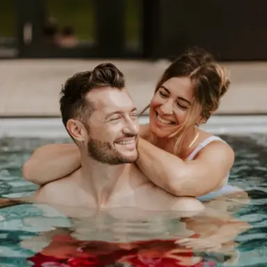 Glückliches Paar entspannt lächelnd im Pool des Klosterhof - Alpine Hideaway & Spa. Wellness-Erlebnis im warmen Wasser.