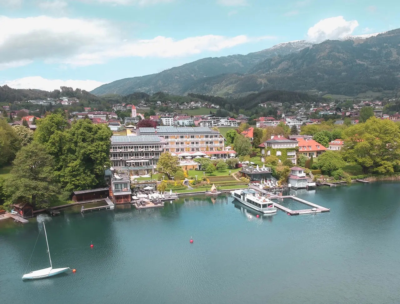Luftaufnahme von KOLLERs Hotel am Millstätter See mit Bergpanorama, eigenem Seezugang und Bootsanlegestelle.