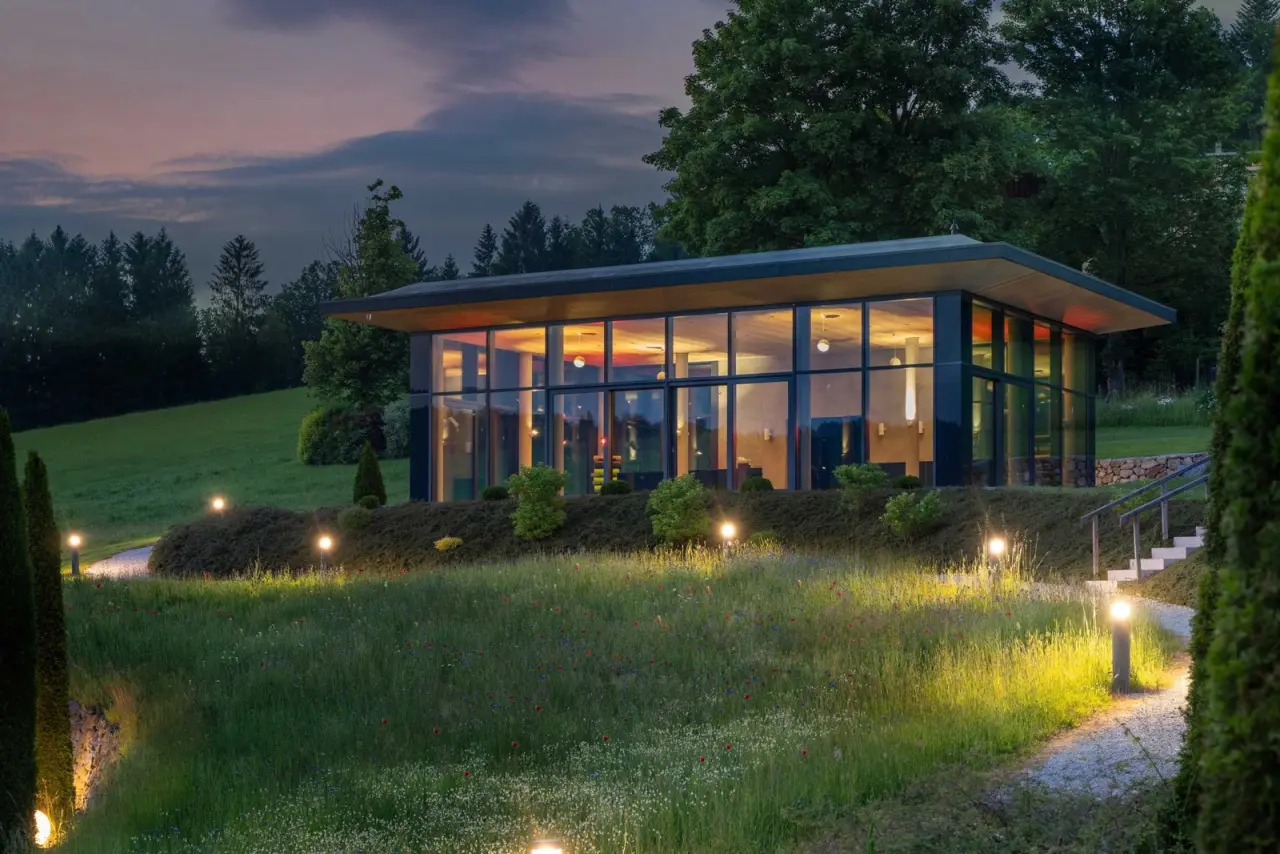 Modernes Glas-Pavillon des Wellnesshotel Lindenwirt im Abendlicht, umgeben von Natur und beleuchteten Wegen.