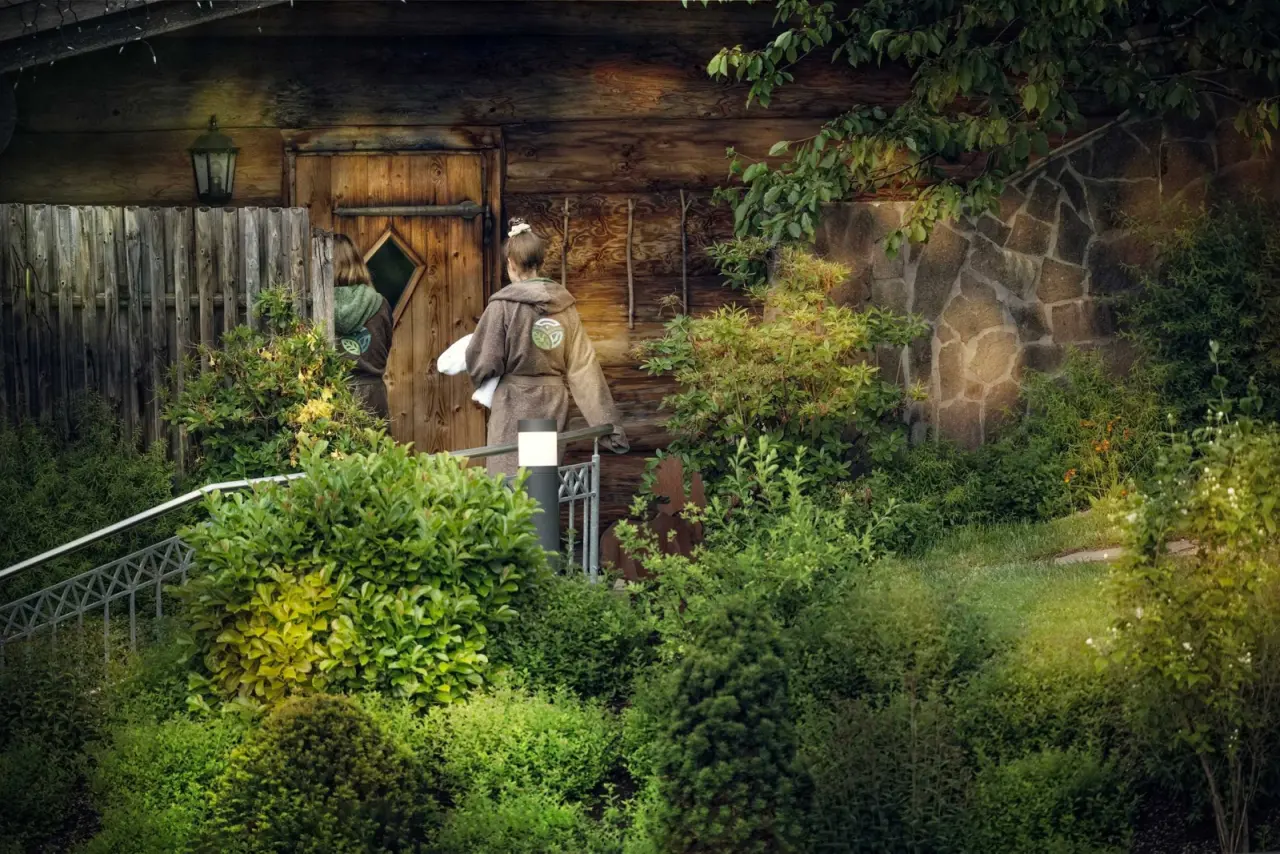 Gäste in Bademänteln auf dem Weg zur rustikalen Sauna im Garten des Wellnesshotel Lindenwirt.