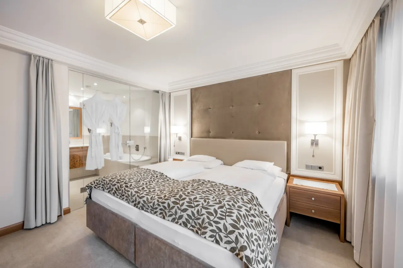 Elegantes Doppelzimmer im Hotel Trofana Royal mit komfortablem Bett und integriertem Bad mit Badewanne und Bademänteln.