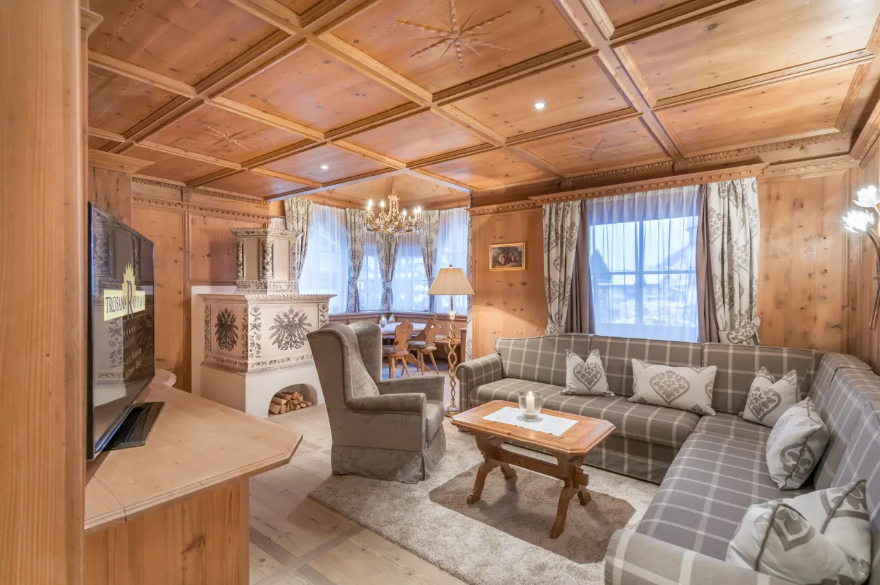 Gemütlicher Wohnbereich einer Suite im Hotel Trofana Royal mit traditionellem Kachelofen, Holztäfelung und bequemer Sitzecke.