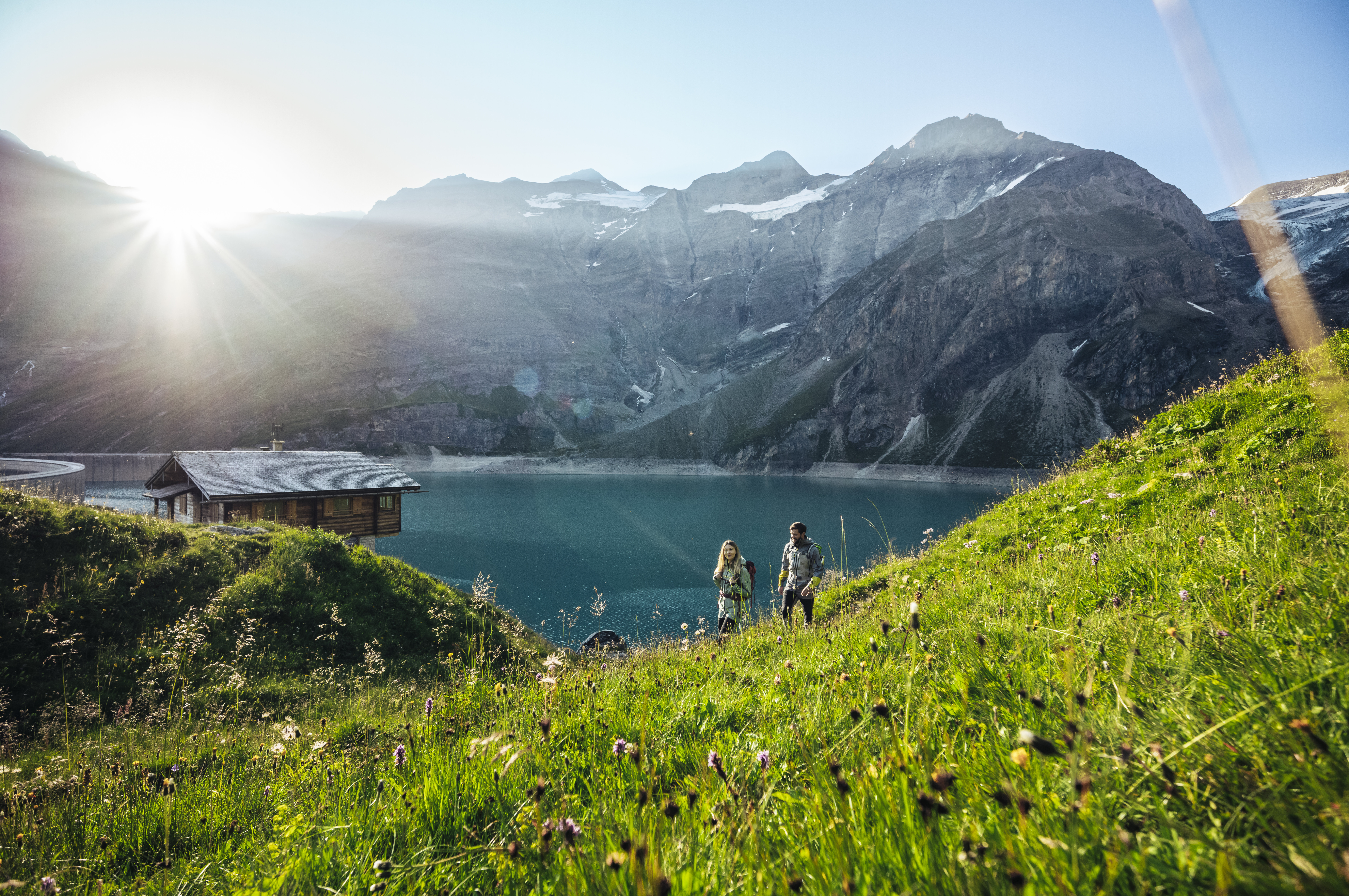 Das Alpenhaus Kaprun in Kaprun – Wanderpaar am Stausee vor imposanter Bergkulisse | Wellnesshotel Salzburger Land