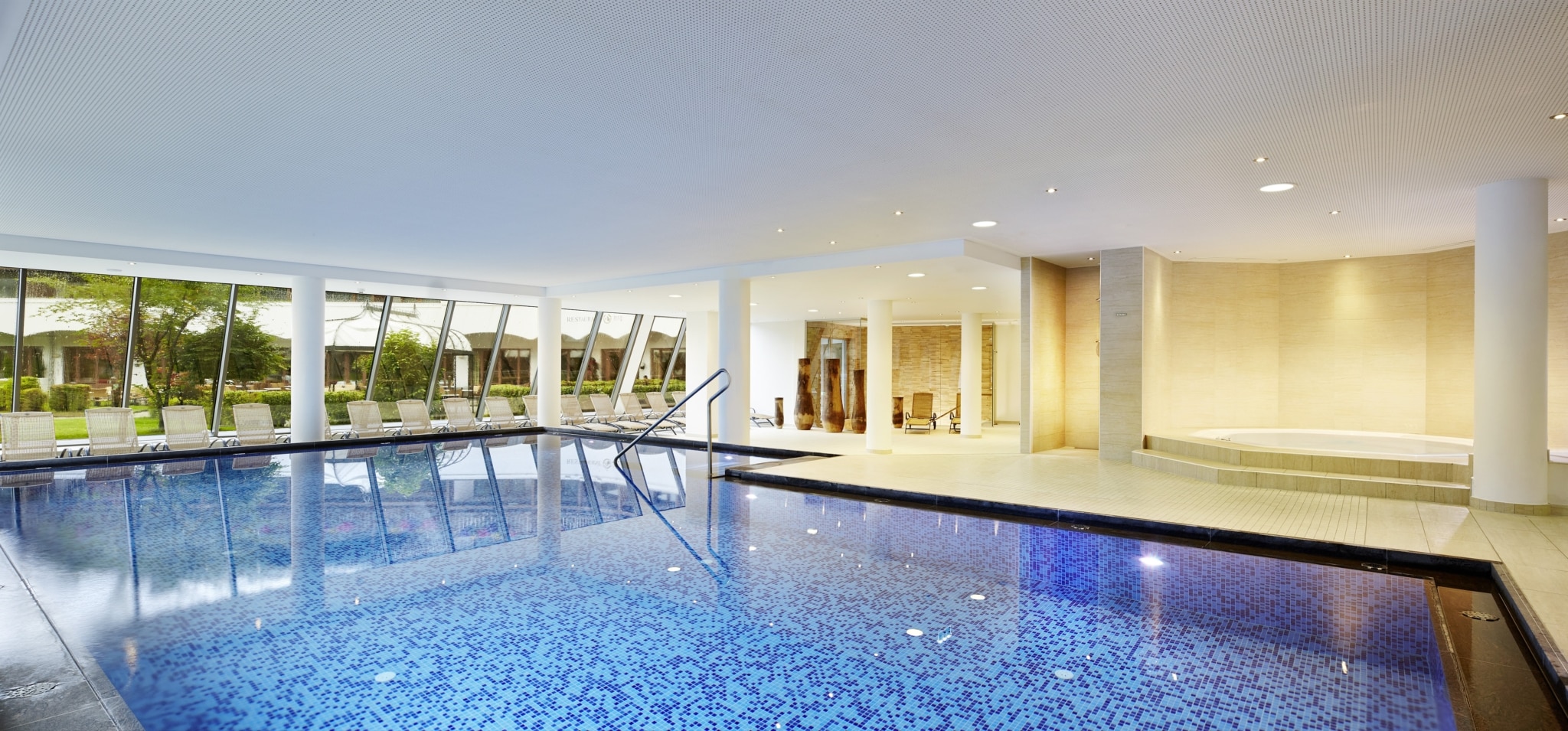 Das Alpenhaus Kaprun in Kaprun – Heller Innenpool mit großen Fenstern und Liegen | Wellnesshotel Salzburger Land