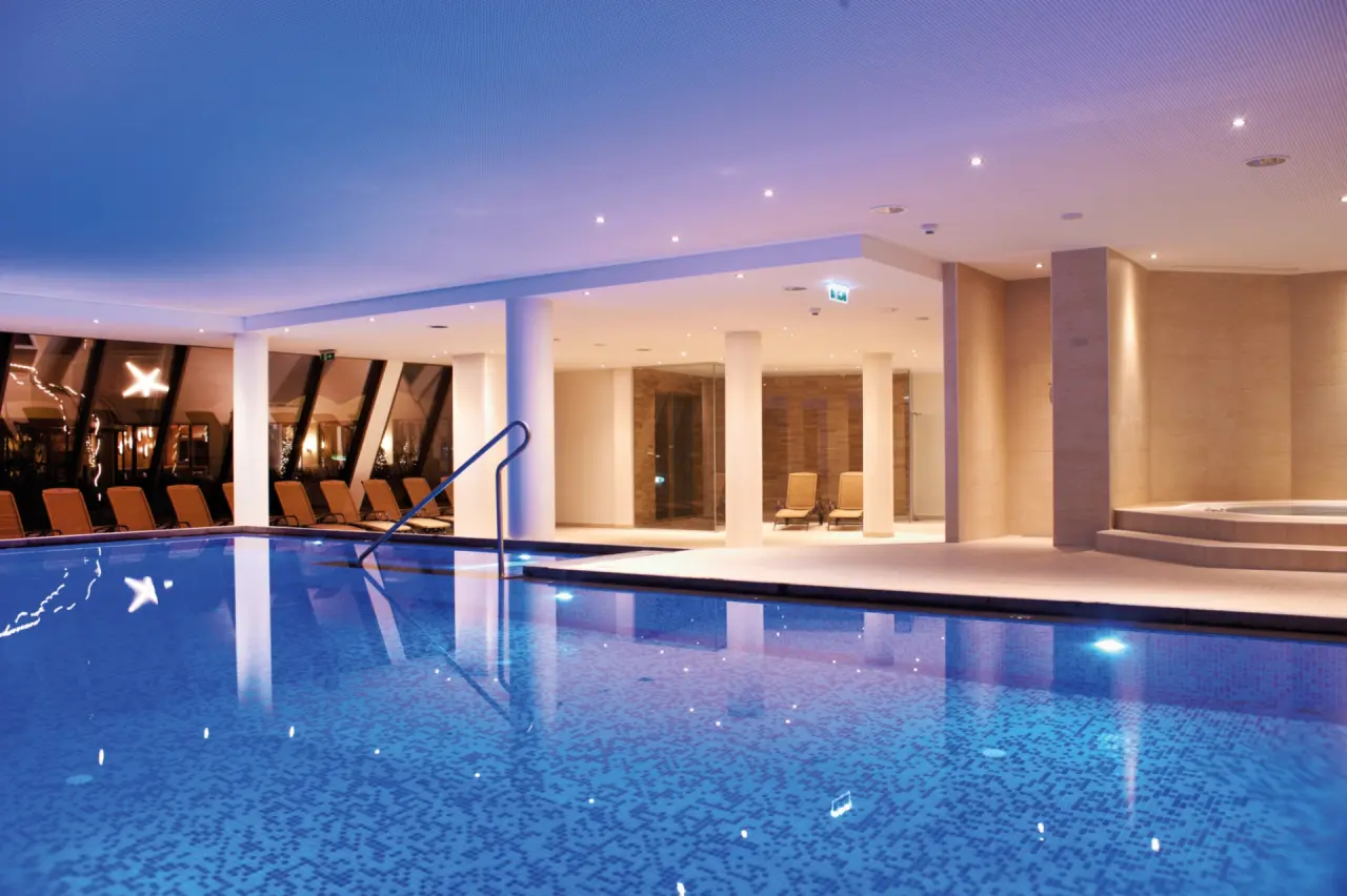 Stilvoller Innenpool mit blauer Beleuchtung und Liegeflächen im Wellnessbereich des Das Alpenhaus Kaprun.