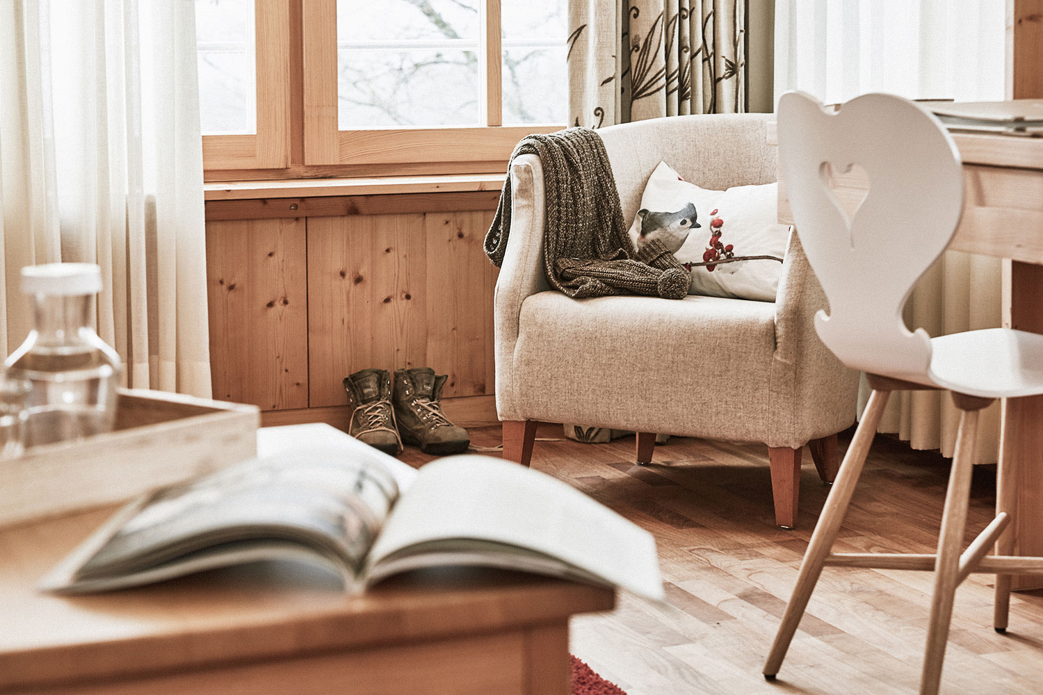 Hotel Die Halde in Oberried-Hofsgrund – Gemütlicher Sessel mit Buch und Stiefeln am Fenster | Wellnesshotel Schwarzwald