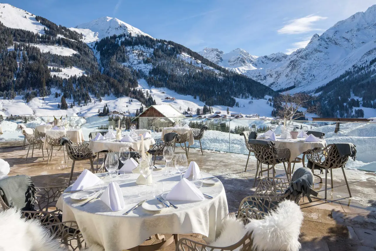 Winterterrasse des Haller's Geniesserhotel mit elegant gedeckten Tischen und atemberaubendem Blick auf die verschneiten Alpen.