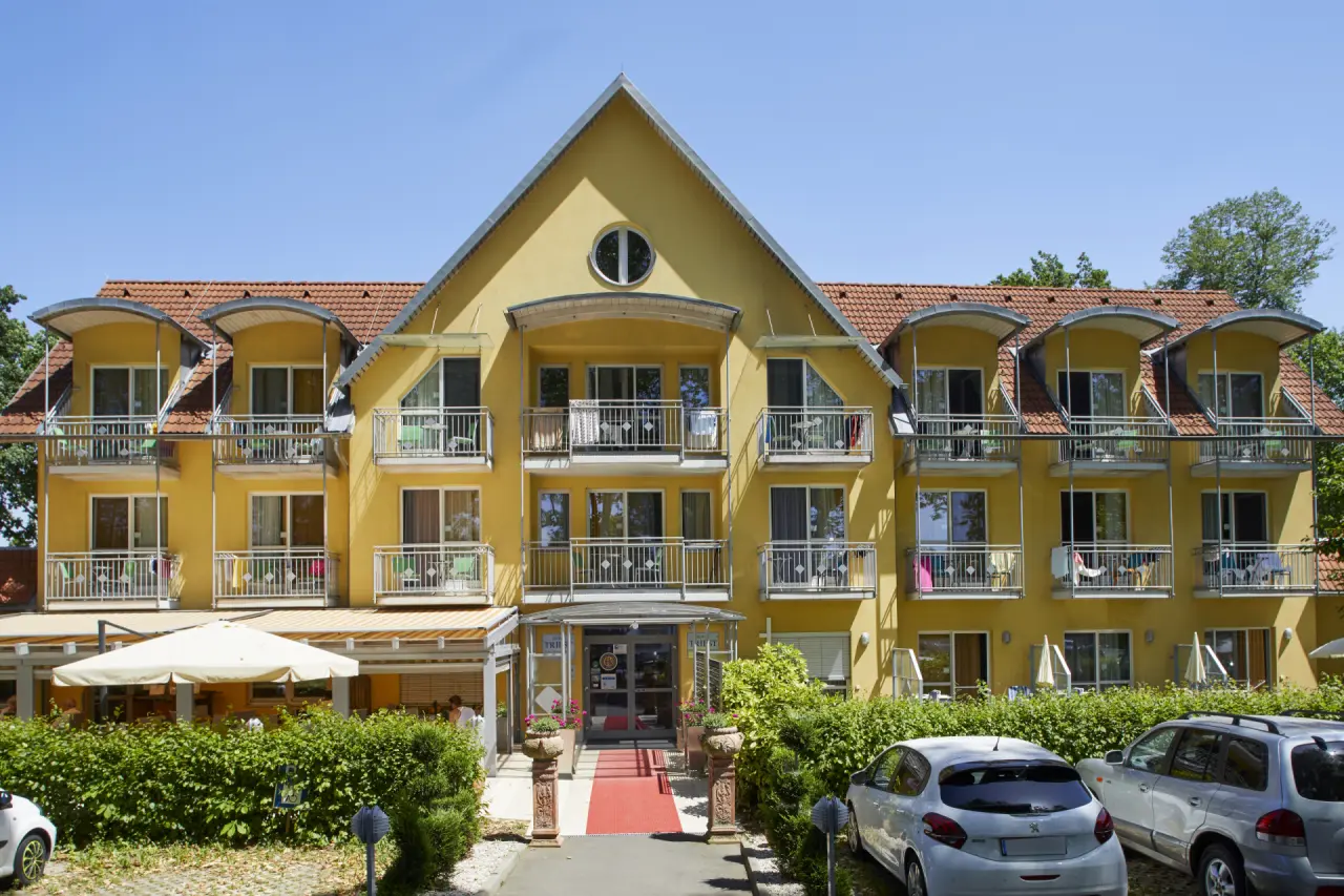Aussenansicht des Kurzentrum Hotel Triest mit gelber Fassade, Balkonen, rotem Teppich und Parkplätzen.