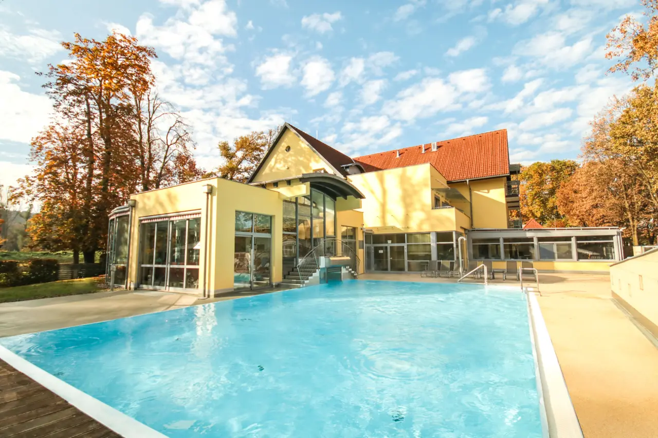 Aussenansicht des Kurzentrum Hotel Triest mit sonnigem Aussenpool und herbstlichen Bäumen. Ideal für Wellnessurlaub.