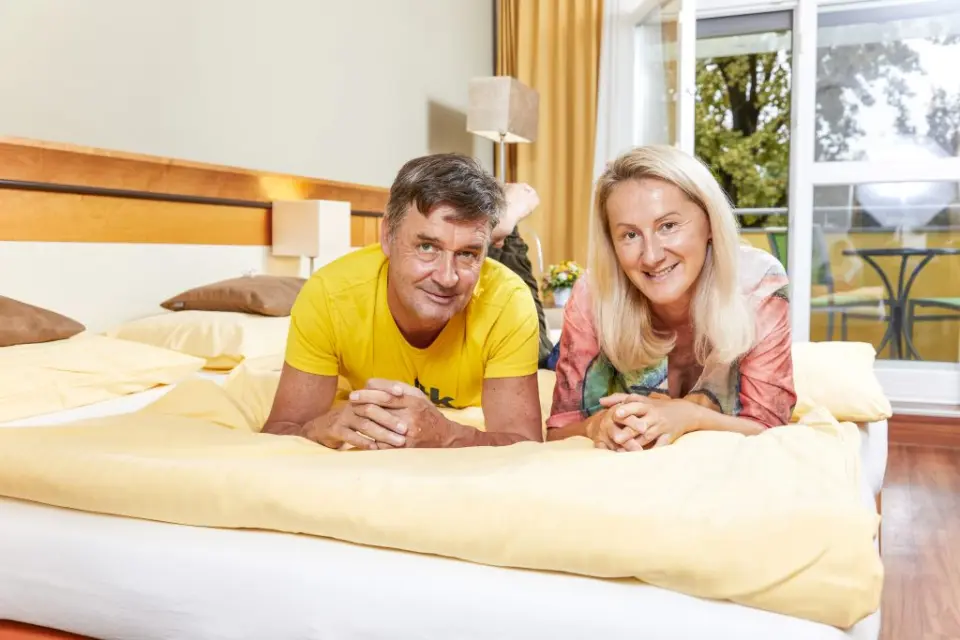 Lachendes Paar entspannt im komfortablen Hotelzimmer mit Balkon im Kurzentrum Hotel Triest.