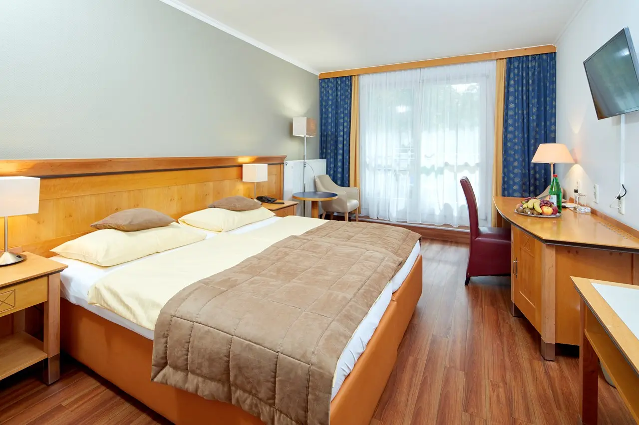 Komfortables Doppelzimmer mit Holzbett, Schreibtisch und Fenster im Kurzentrum Hotel Triest.