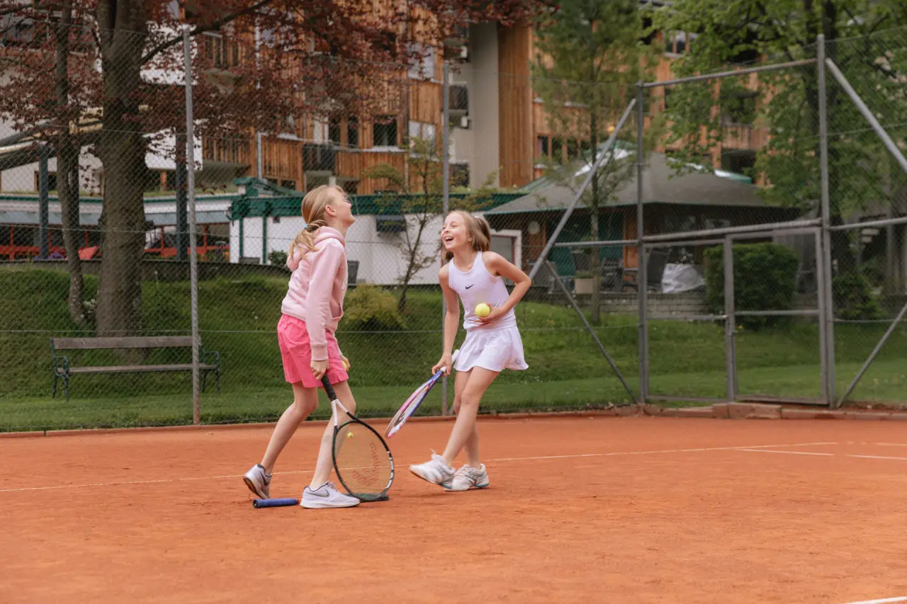 Hotel DIE POST in Bad Kleinkirchheim – Zwei Mädchen spielen fröhlich Tennis auf dem Außenplatz | Wellnesshotel Kärnten